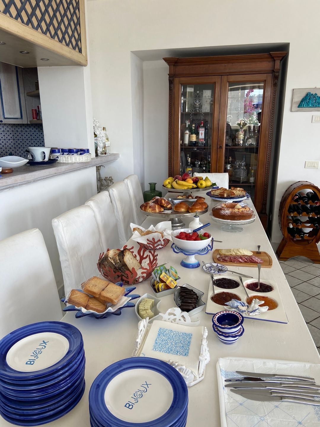 An elegantly arranged breakfast spread featuring pastries, fresh fruits, cured meats, spreads, and locally-themed blue and white dishware on a white dining table.