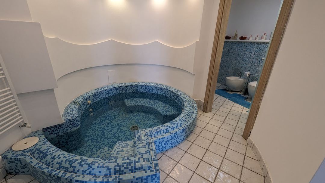 A curved, kidney-shaped indoor hot tub with blue mosaic tile design in a spa bathroom.