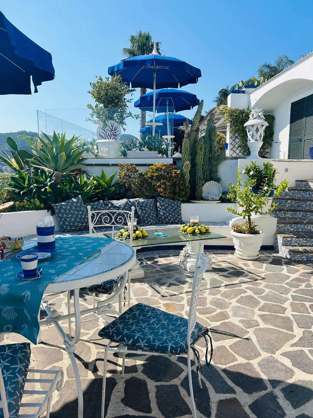 Mediterranean-style outdoor terrace with blue umbrellas, white furnishings, potted plants, and sea views at Relais Bijoux on Ischia.